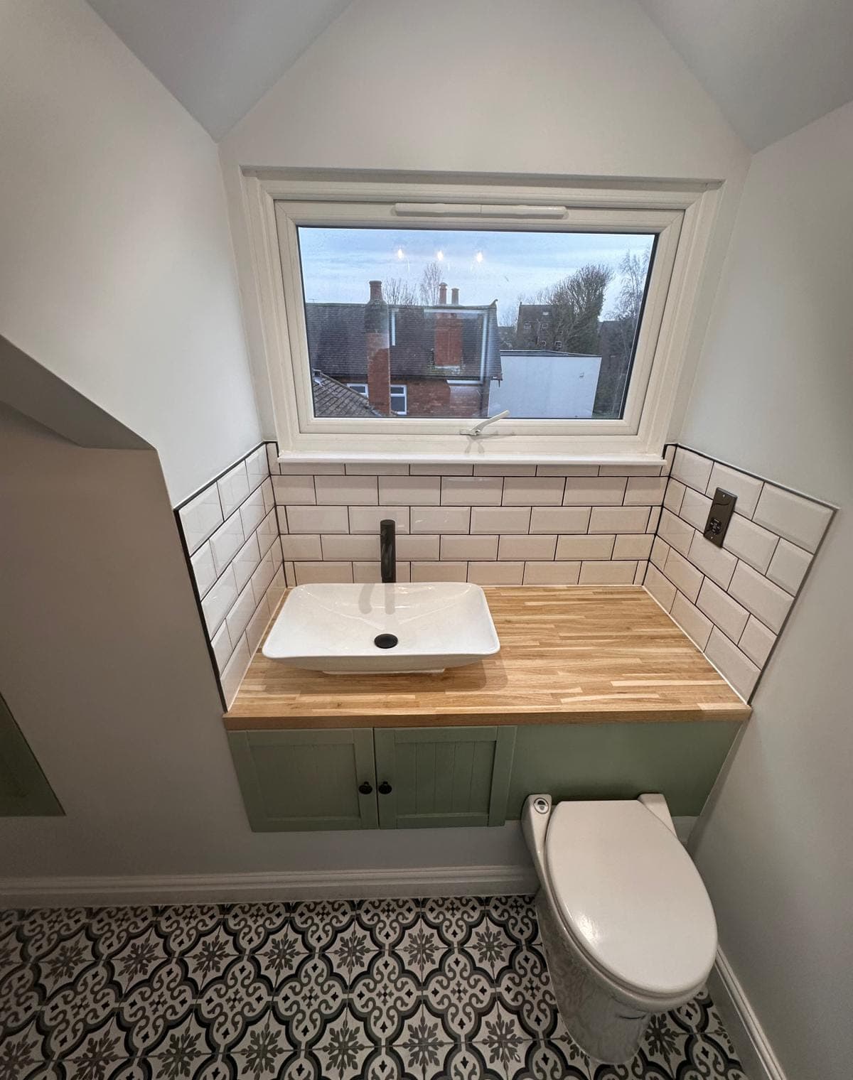 A bathroom vanity: a counter-top basin on a solid timber top over green shaker doors