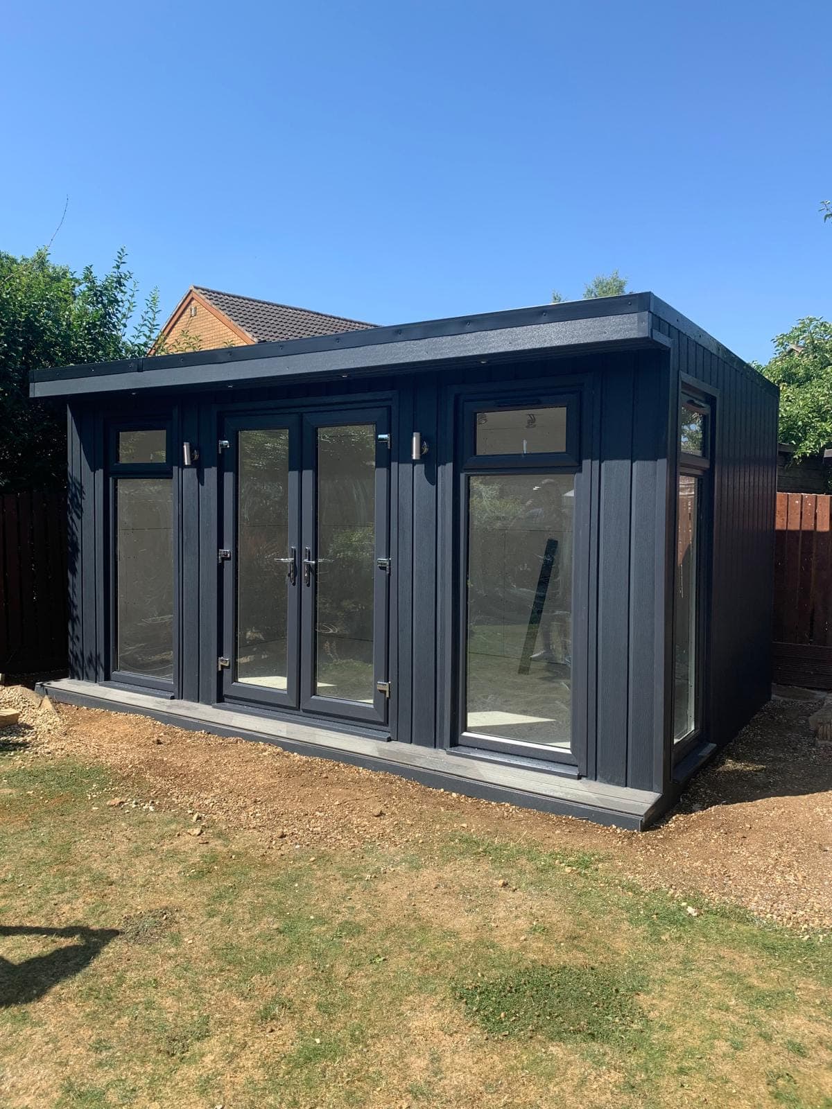 A dark grey clad garden room with French doors and side windows, set on a level base