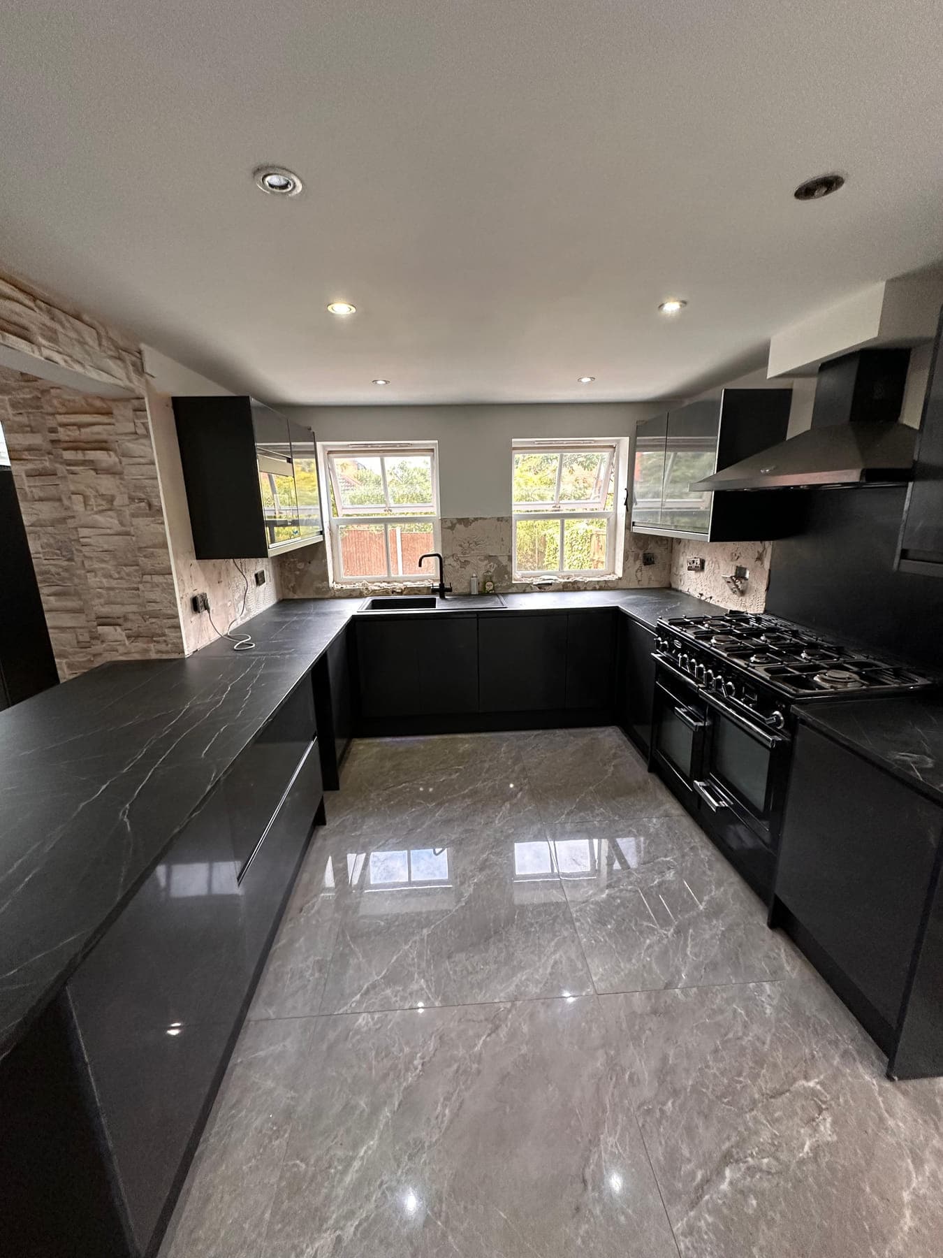 A dark handleless kitchen in a U-shape with a stone worktop, range cooker and split-face stone wall